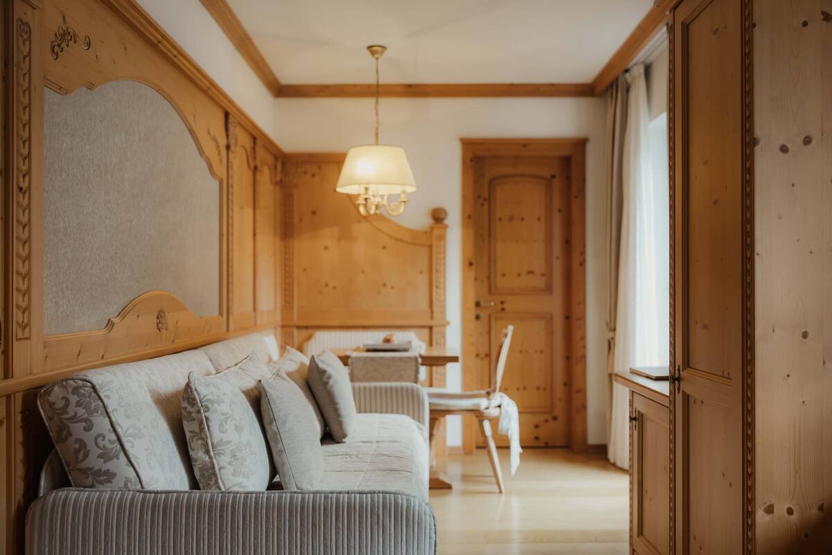 A room with a wooden headboard, a sofa with patterned cushions, a table, and a chair.