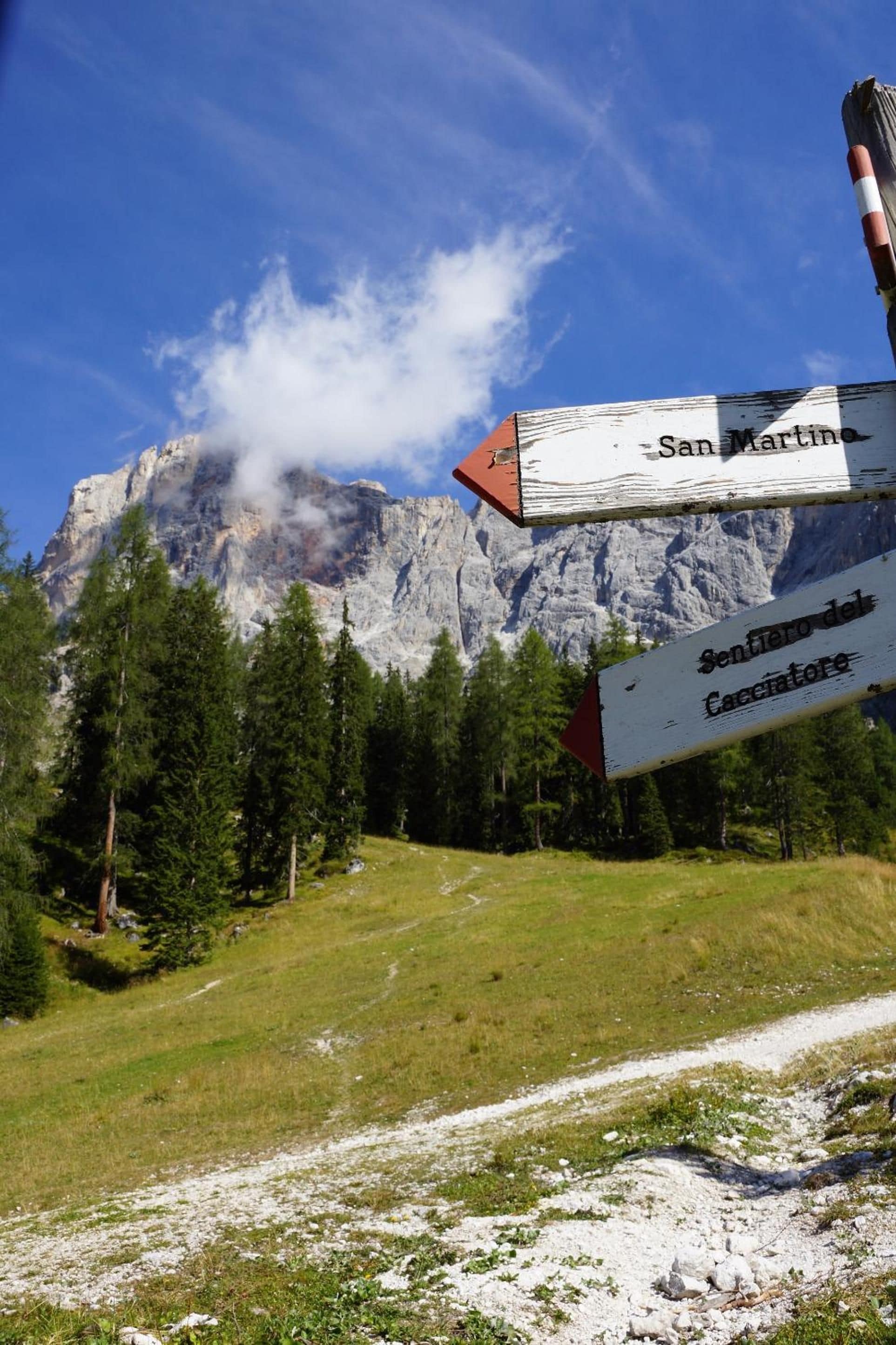 A mountain landscape with a signpost indicating directions to San Martino and Sentiero del Caccinatore.