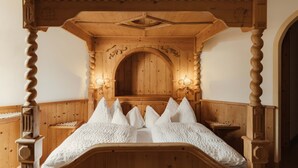 A wooden four-poster bed with a carved headboard, a wooden bench, and wall-mounted sconces. - Hotel Colbricon  (Primiero San Martino di Castrozza)