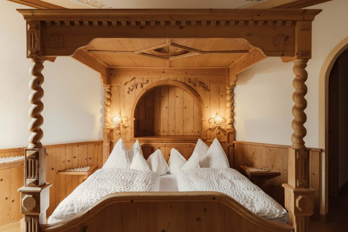 A wooden four-poster bed with a carved headboard, a wooden bench, and wall-mounted sconces.