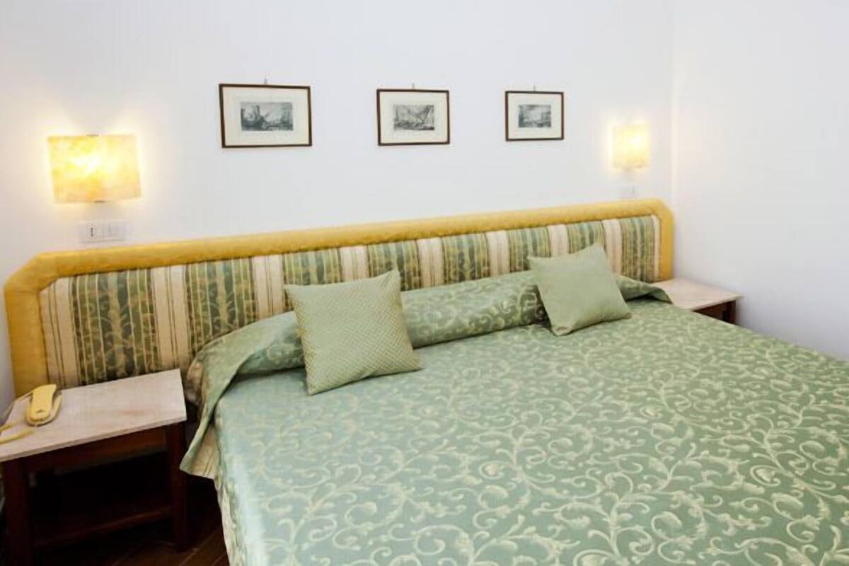 Une chambre à coucher avec un lit, deux tables de chevet et trois tableaux encadrés accrochés au mur.