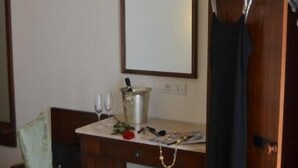 Ein Hotelzimmer mit einem Holztisch, einem Spiegel, einem aufgehängten Kleid und einem Paar Schuhe auf dem Boden.