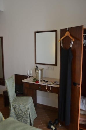 Une chambre d’hôtel avec un bureau en bois, un miroir, une robe suspendue et une paire de chaussures posées sur le sol.