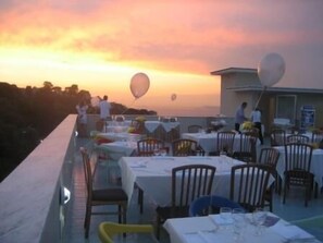 Un espace de restauration en plein air, avec des tables et des chaises, offrant une vue panoramique sur un magnifique coucher de soleil.