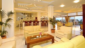 Un amplio vestíbulo de hotel con una zona de estar central, un bar y una escalera que conduce a los pisos superiores.