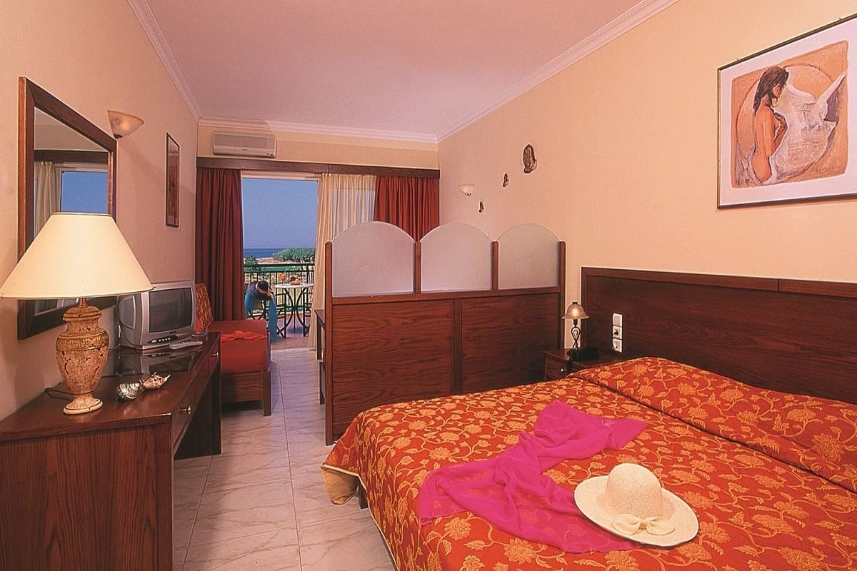 A hotel room with a bed, a television, a desk with a lamp, and a window with curtains.
