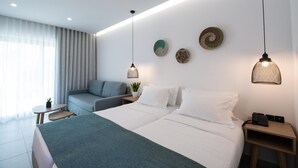 A modern hotel room with a large bed, a sofa, a small table, and decorative wall art. - Selini Suites (Platanias)