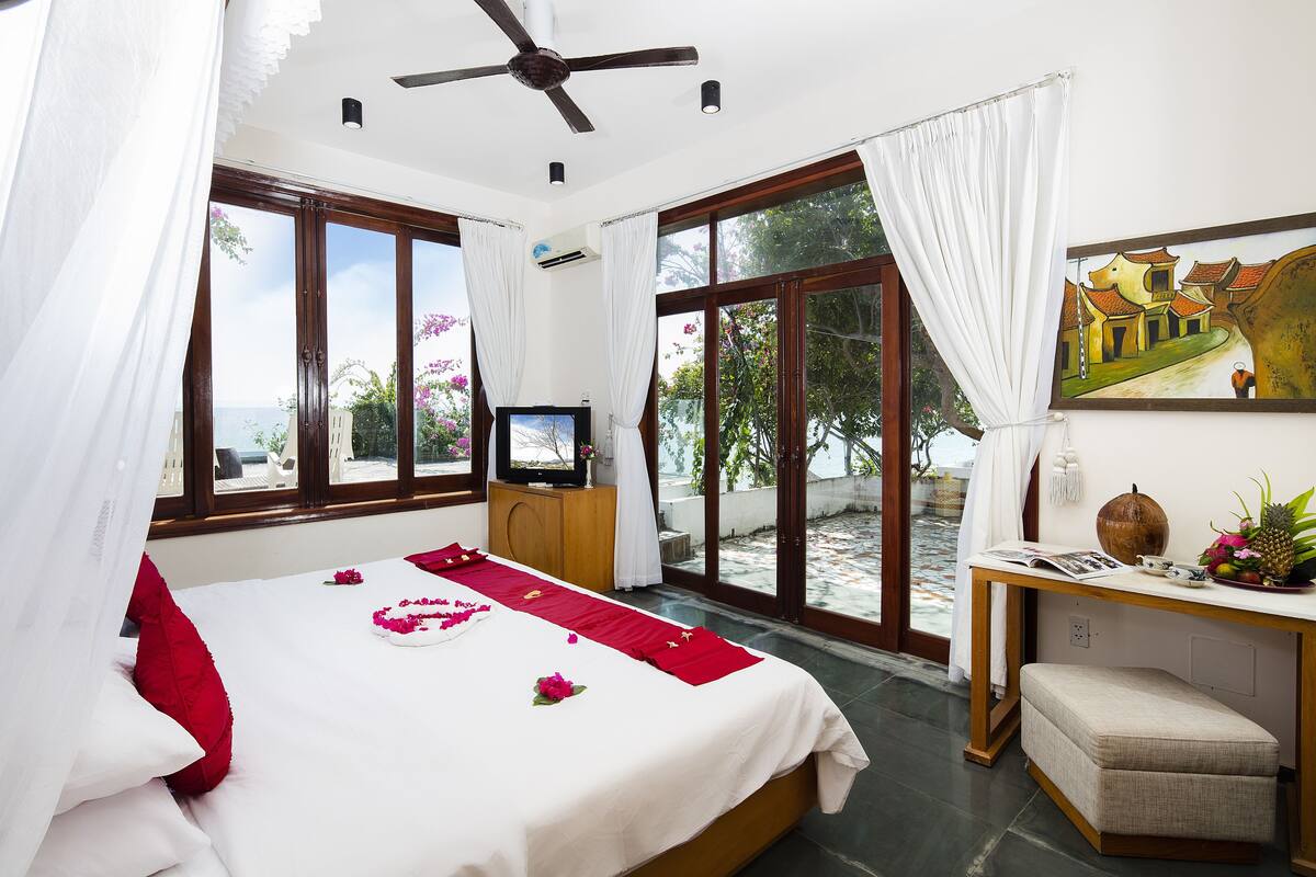 A room with a bed, a desk, a television, and a large window with curtains.