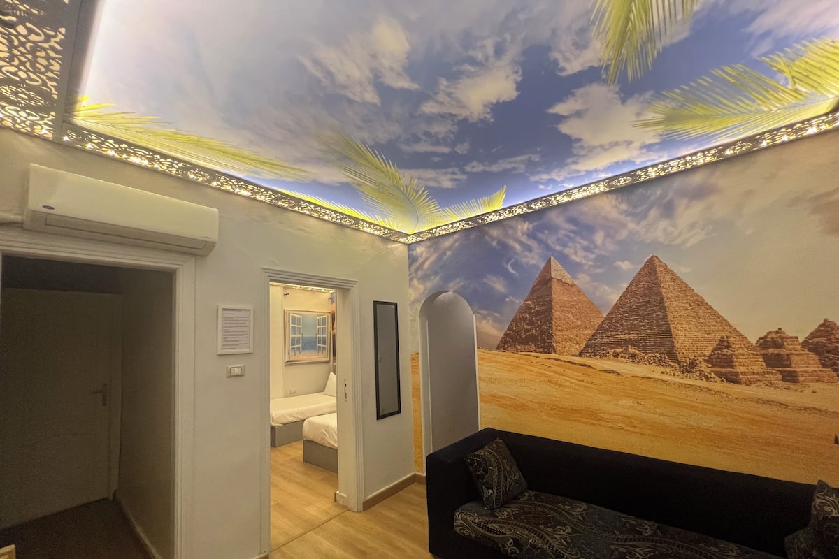 A room with a mural of pyramids, a sofa, and a bed.