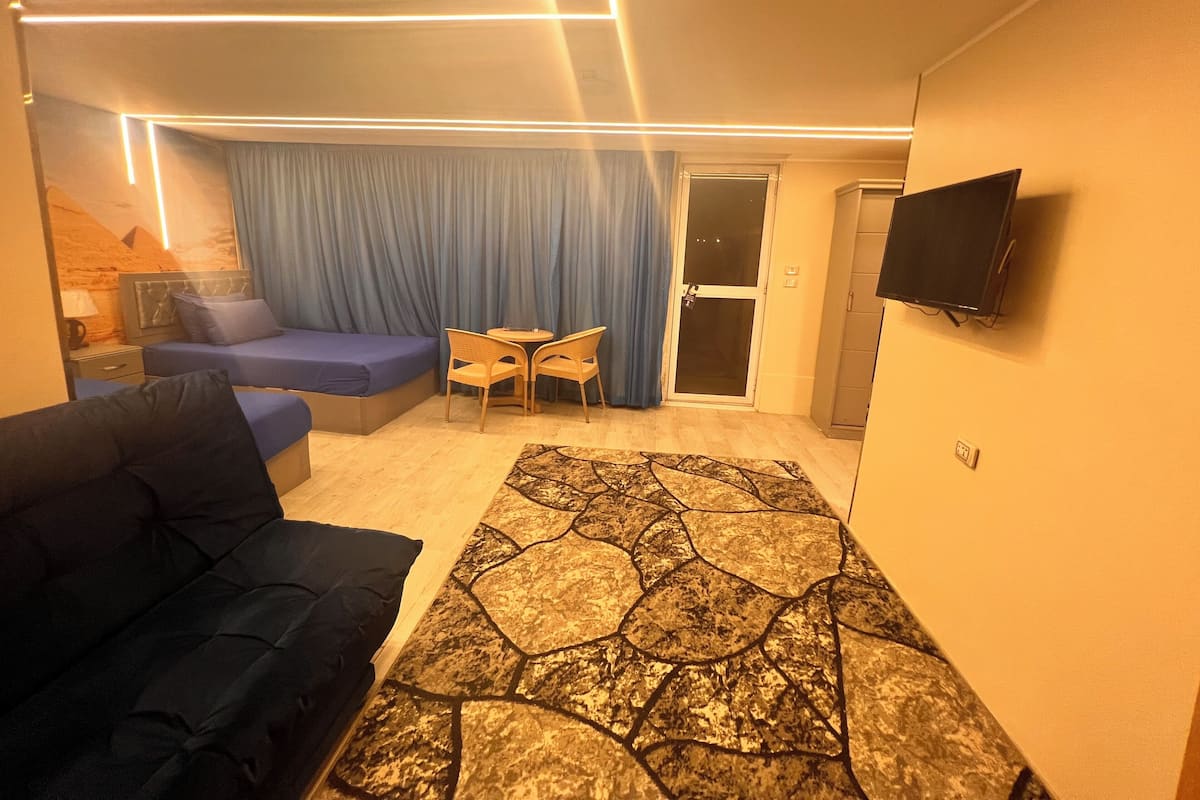 A hotel room with a sofa, a small table with chairs, a TV mounted on the wall, and a curtain-covered door.