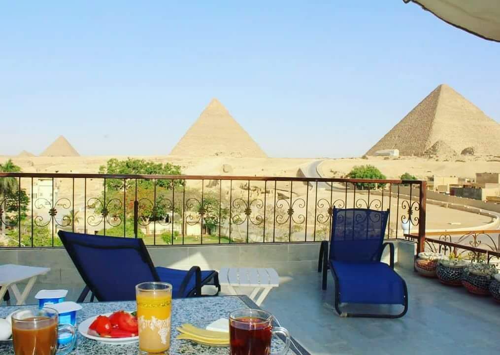 A balcony with a table, chairs, and drinks, overlooking the pyramids.