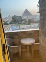Un balcón con sillas de mimbre y una mesa redonda, con vista a pirámides y un paisaje desértico.