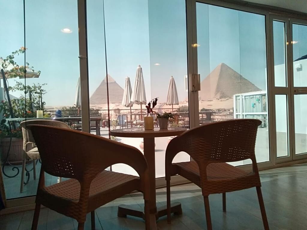 A view of the pyramids through large windows with wicker chairs and a table in the foreground.