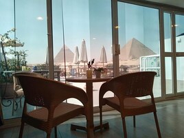 A view of the pyramids through large windows with wicker chairs and a table in the foreground.