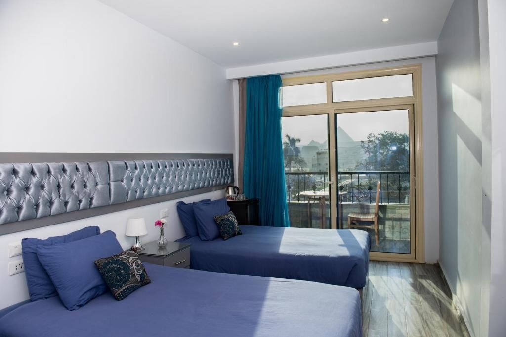 A hotel room with two beds, a large window with a view, and a balcony.