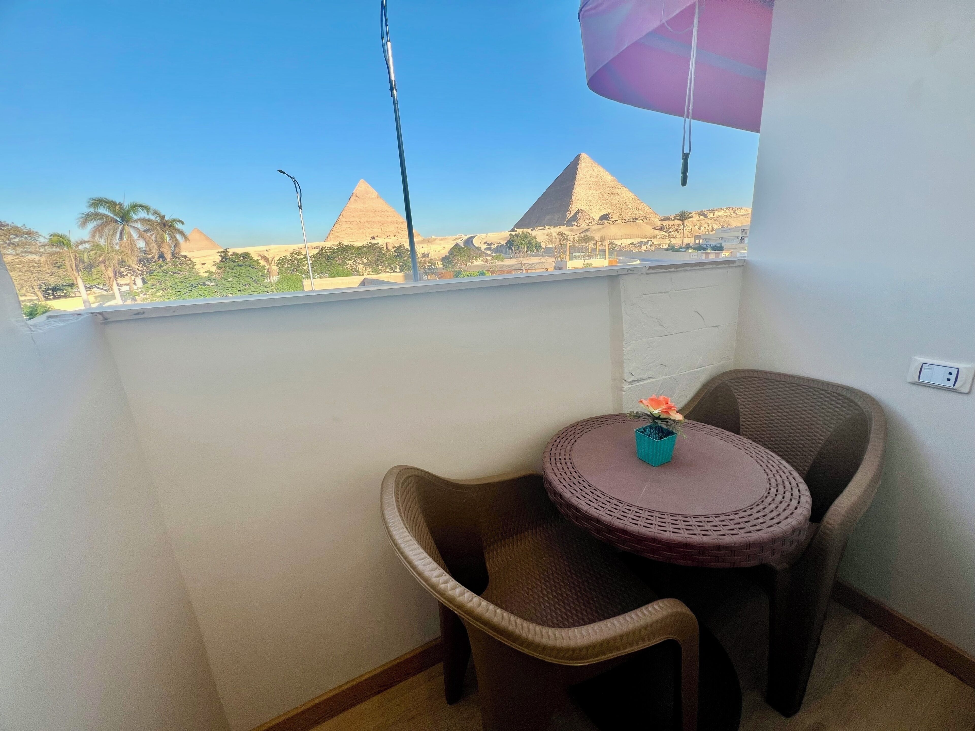Un balcon avec des fauteuils en osier, une petite table et une vue sur les pyramides.