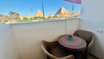 Un balcon avec des fauteuils en osier, une petite table et une vue sur les pyramides.