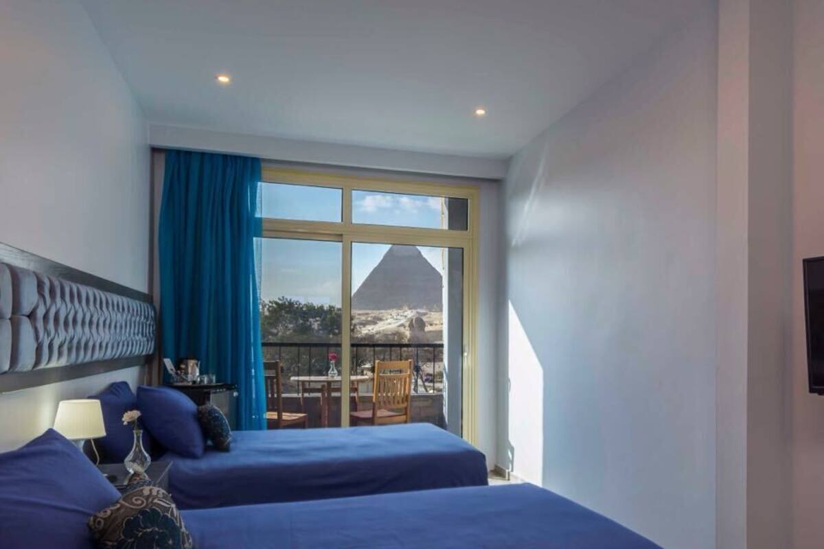 A hotel room with two beds, a large window with a view of a pyramid, and a television on the wall.