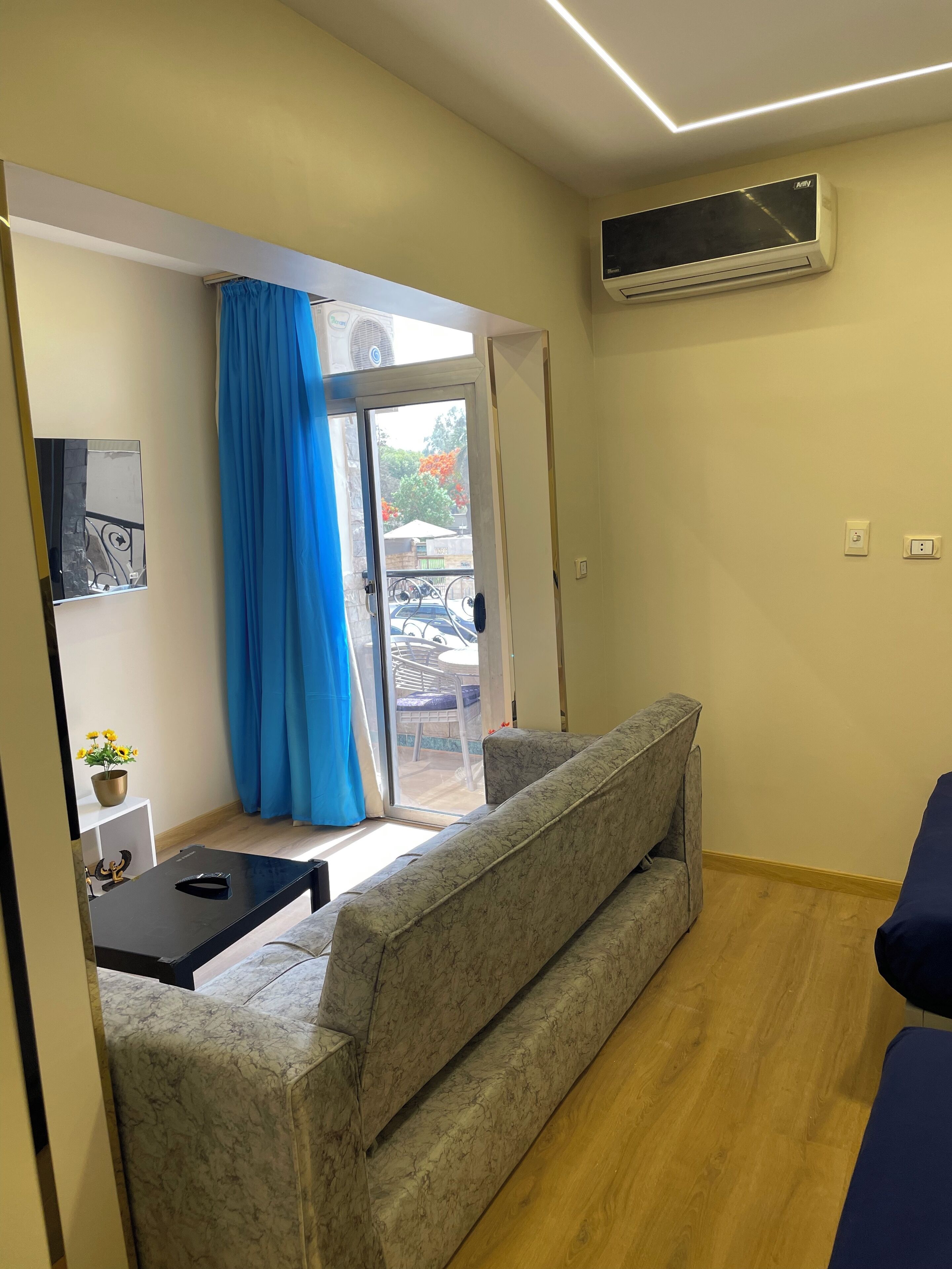 Ein modernes Wohnzimmer mit einem sofa in Marmoroptik, einem kleinen Tisch mit einer Pflanze und einer Glastür, die zu einem Außenbereich mit einer Terrasse führt.