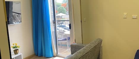 Una sala moderna con un sofá estampado en mármol, una mesita con una planta y un ventanal corredero que da a un área exterior con patio.