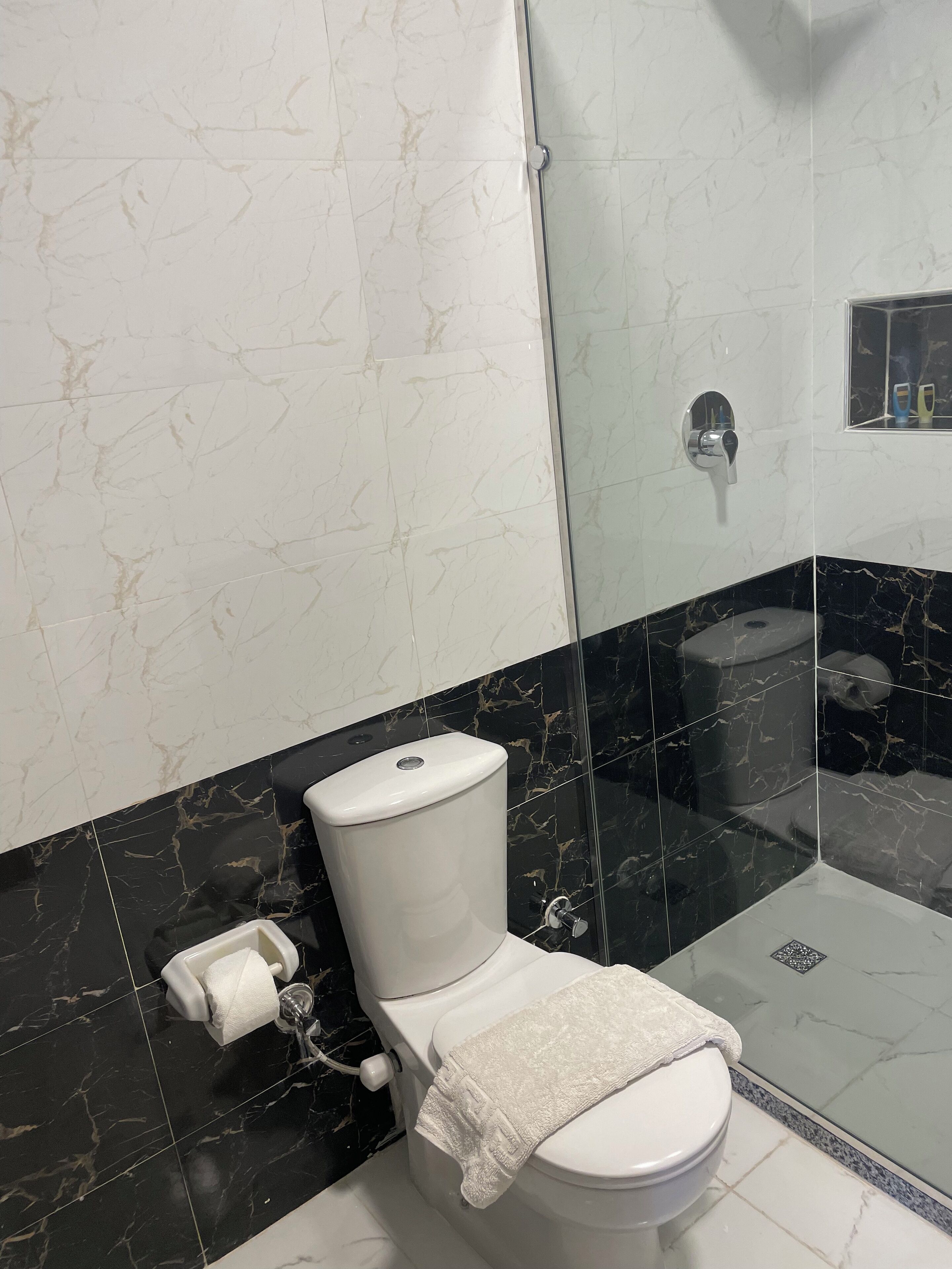A modern bathroom with a toilet, a glass shower enclosure, and marble-patterned walls.