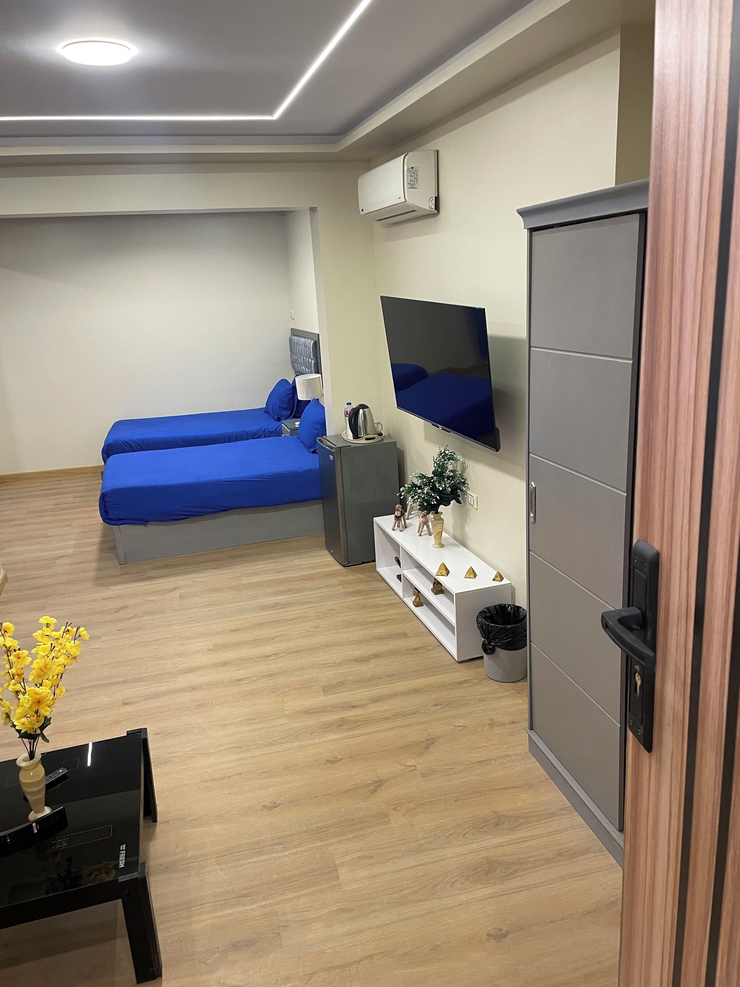 A hotel room with two beds, a TV mounted on the wall, a minibar, and a wooden floor.