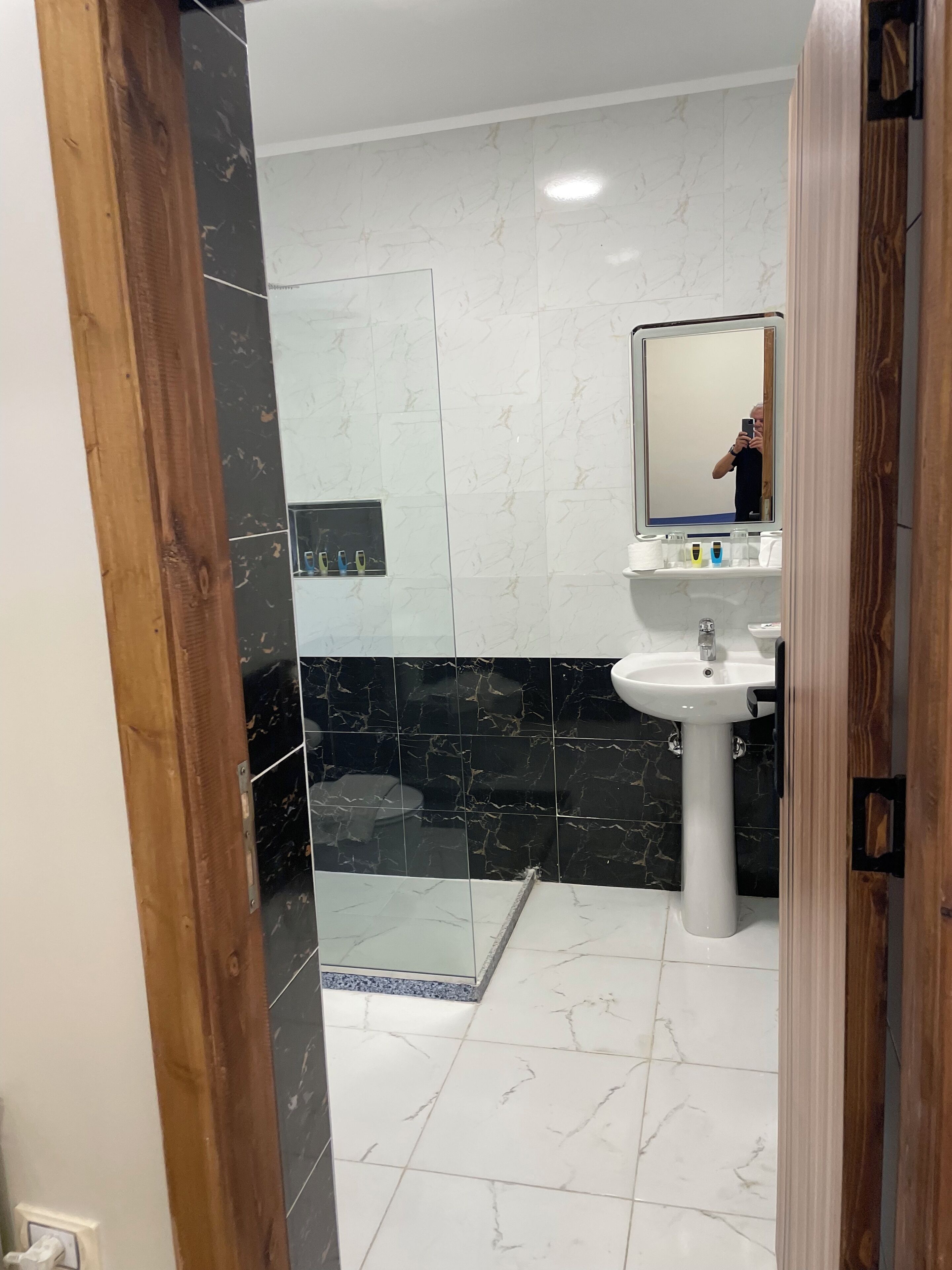 Een moderne badkamer met een wit wastafelmeubel, zwarte marmeren tegels en een glazen douchecabine.