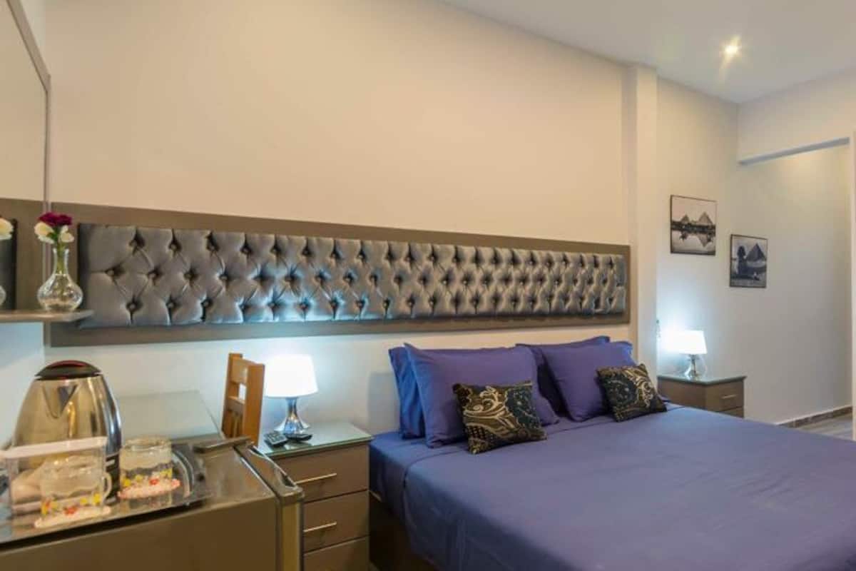 A bedroom with a large bed, a tufted headboard, a nightstand with a lamp, and a wardrobe.