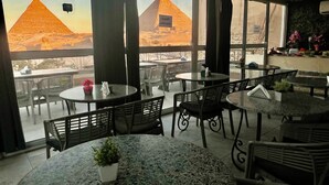 A restaurant with outdoor seating, featuring tables and chairs, and a view of pyramids in the background. - Pyramids View inn Bed & Breakfast (Giza)