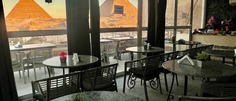 Un restaurante con terraza, que cuenta con mesas y sillas, y vistas a las pirámides de fondo.