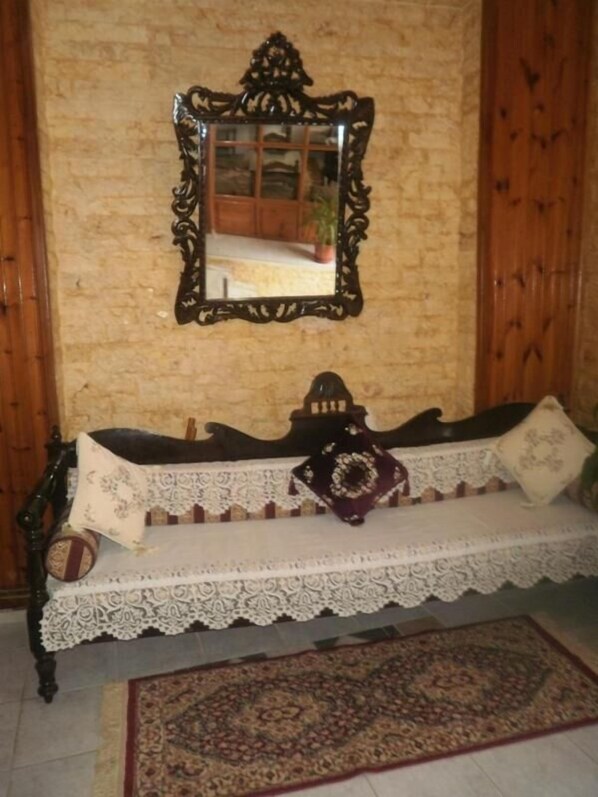 A room with a wooden bench, a lace tablecloth, a patterned rug, and a mirror with a wooden frame. - Regina Hotel (Skopelos)
