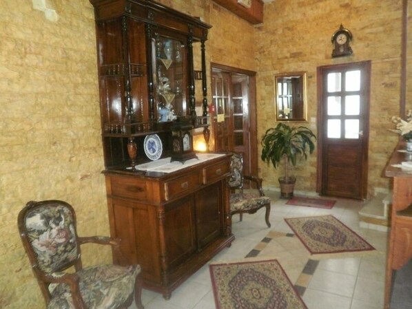A traditional room with a wooden cabinet, a desk, a chair, a potted plant, and a door with a mirror. - Regina Hotel (Skopelos)
