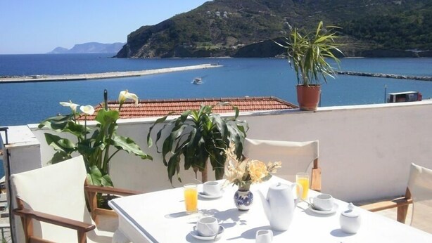Una terraza con una mesa dispuesta para el desayuno, con vistas al mar y a las montañas costeras.