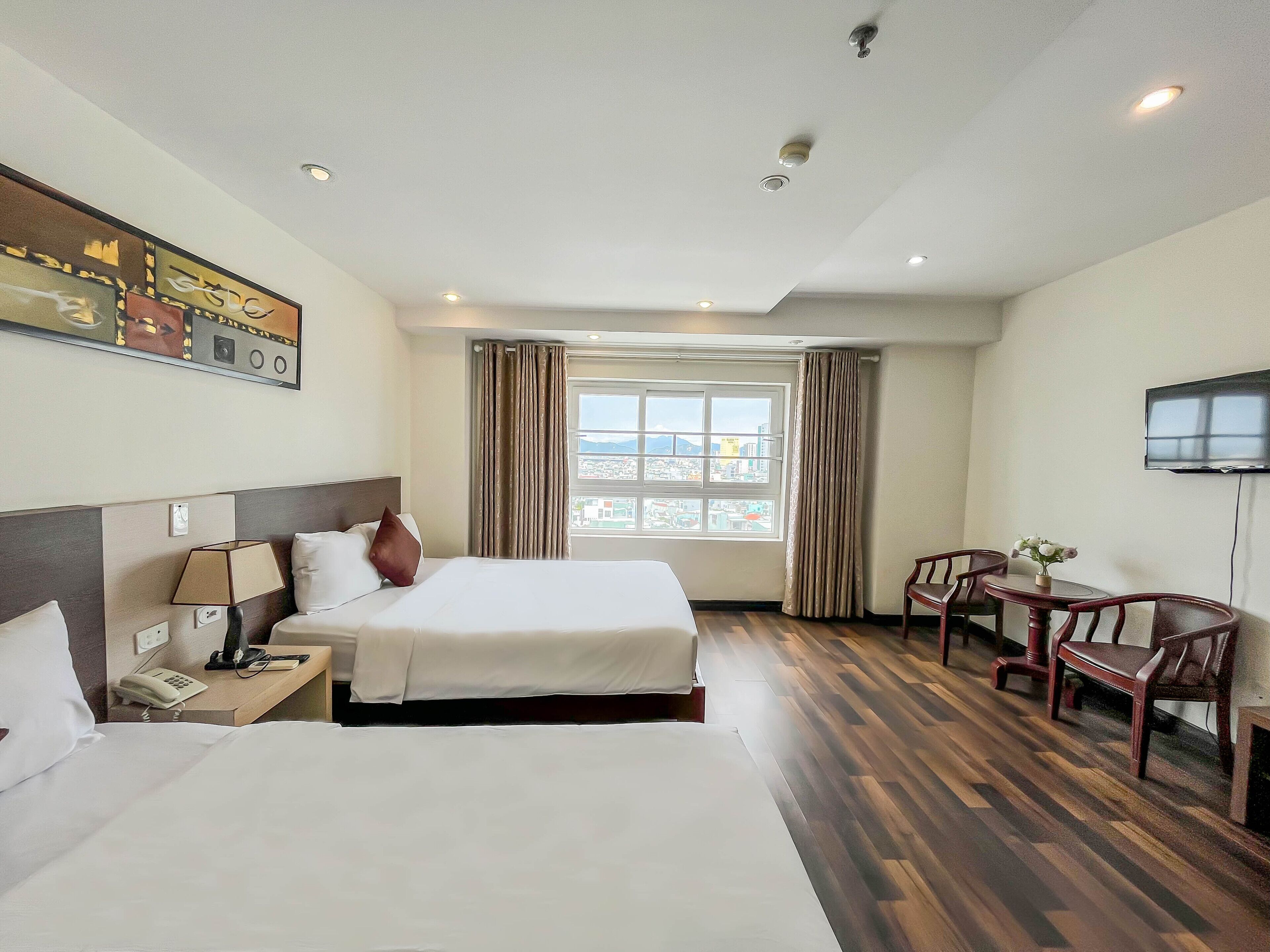 A hotel room with two beds, a desk with a telephone, a TV, and a window with curtains.