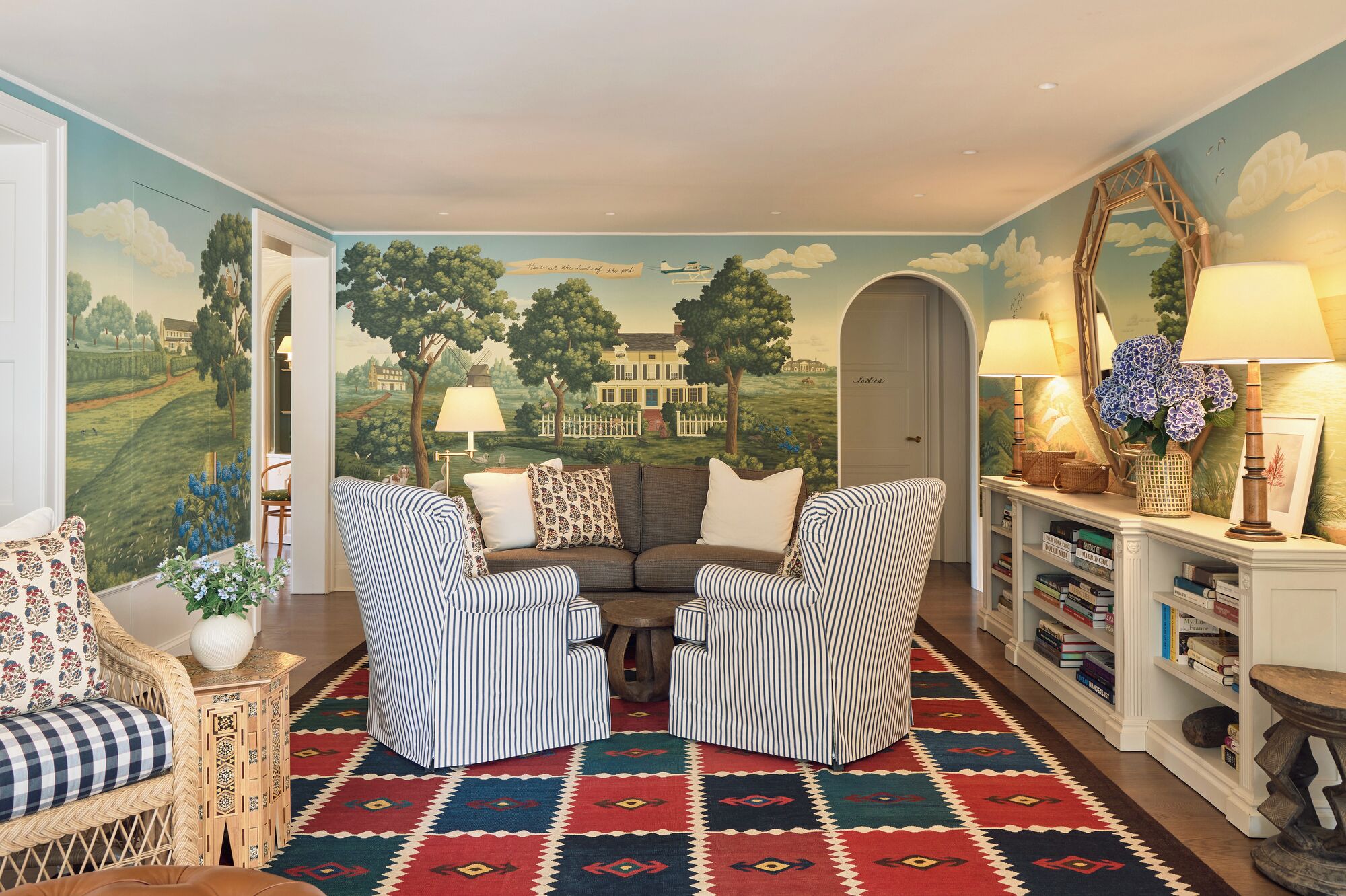 Una sala de estar acogedora con un mural, sillones a rayas, un sofá, una alfombra estampada y una estantería.