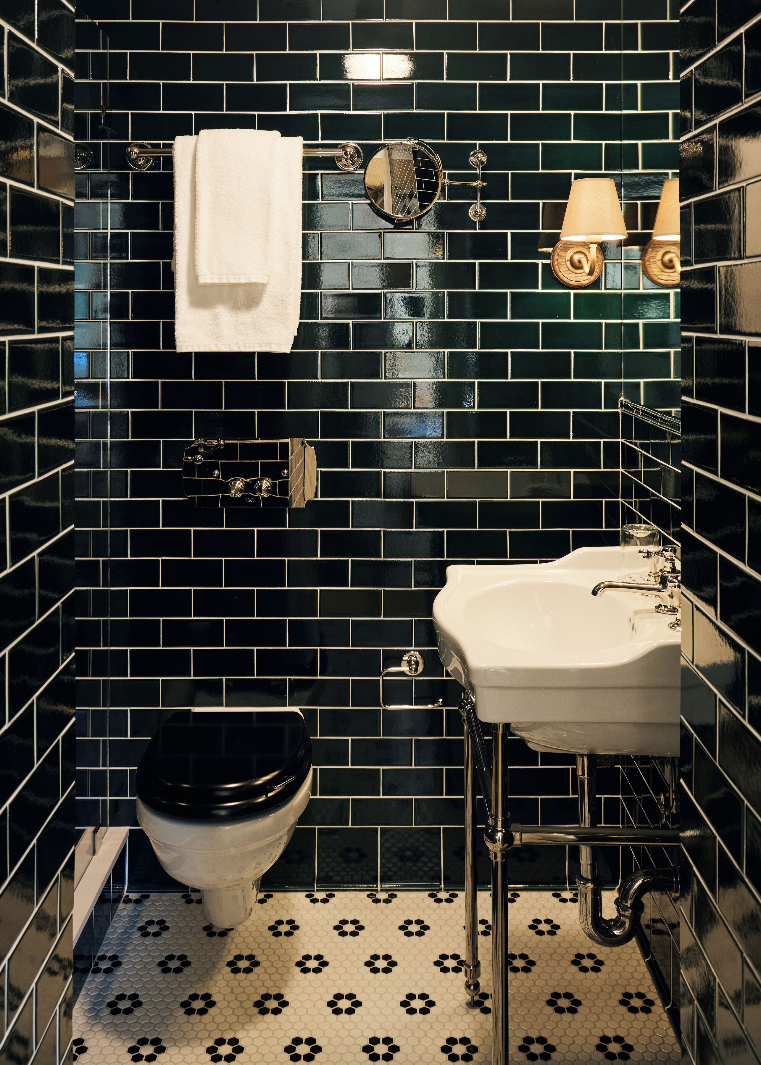 Un baño con paredes de azulejos negros, un inodoro blanco, un lavabo blanco y un espejo.