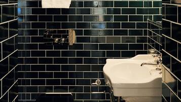 Un baño con paredes de azulejos negros, un inodoro blanco, un lavabo blanco y un espejo.