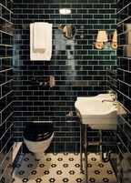 Un baño con paredes de azulejos negros, un inodoro blanco, un lavabo blanco y un espejo.