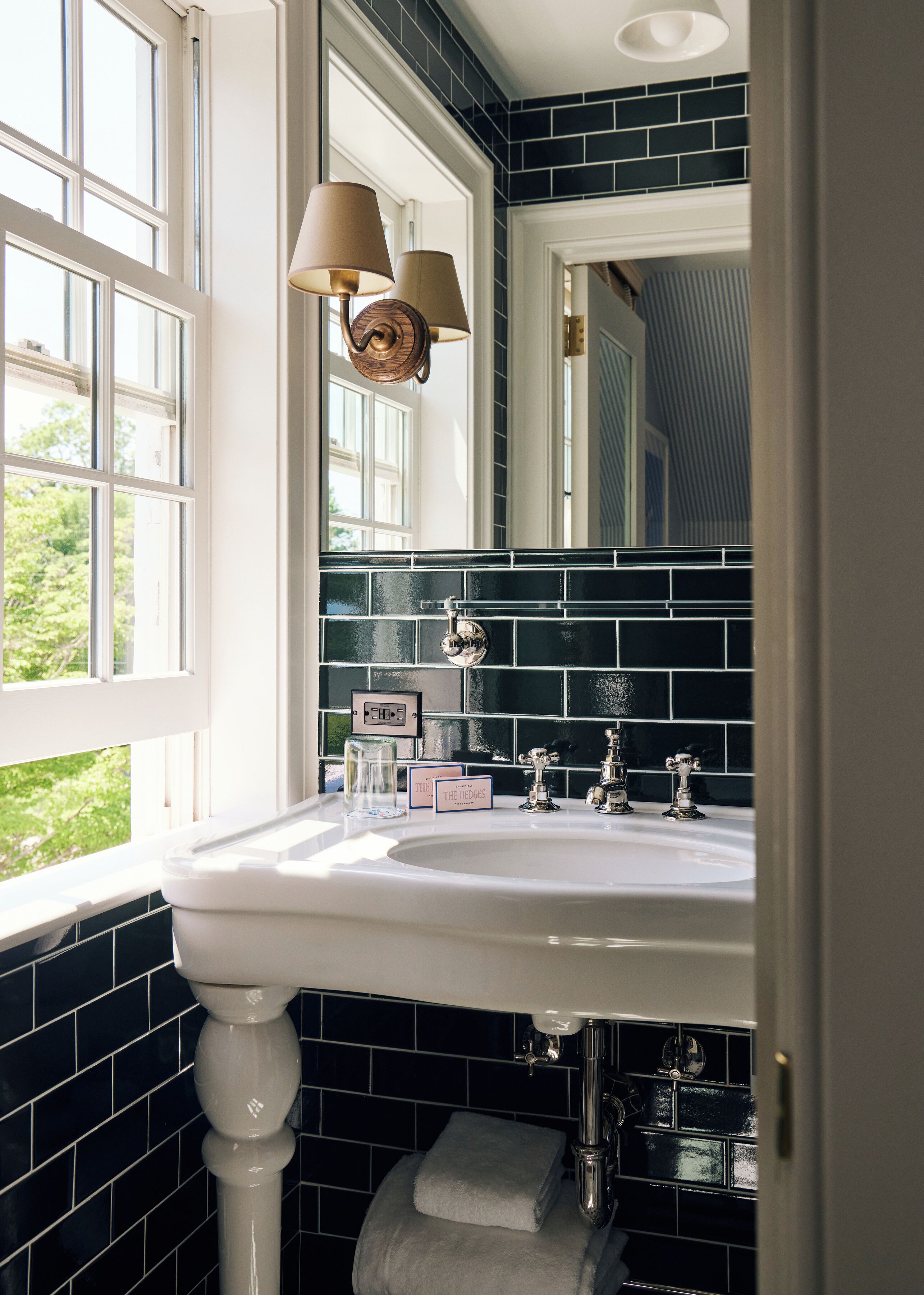 A bathroom with a white sink, black tiled walls, a window with white frames, and a mirror above the sink.