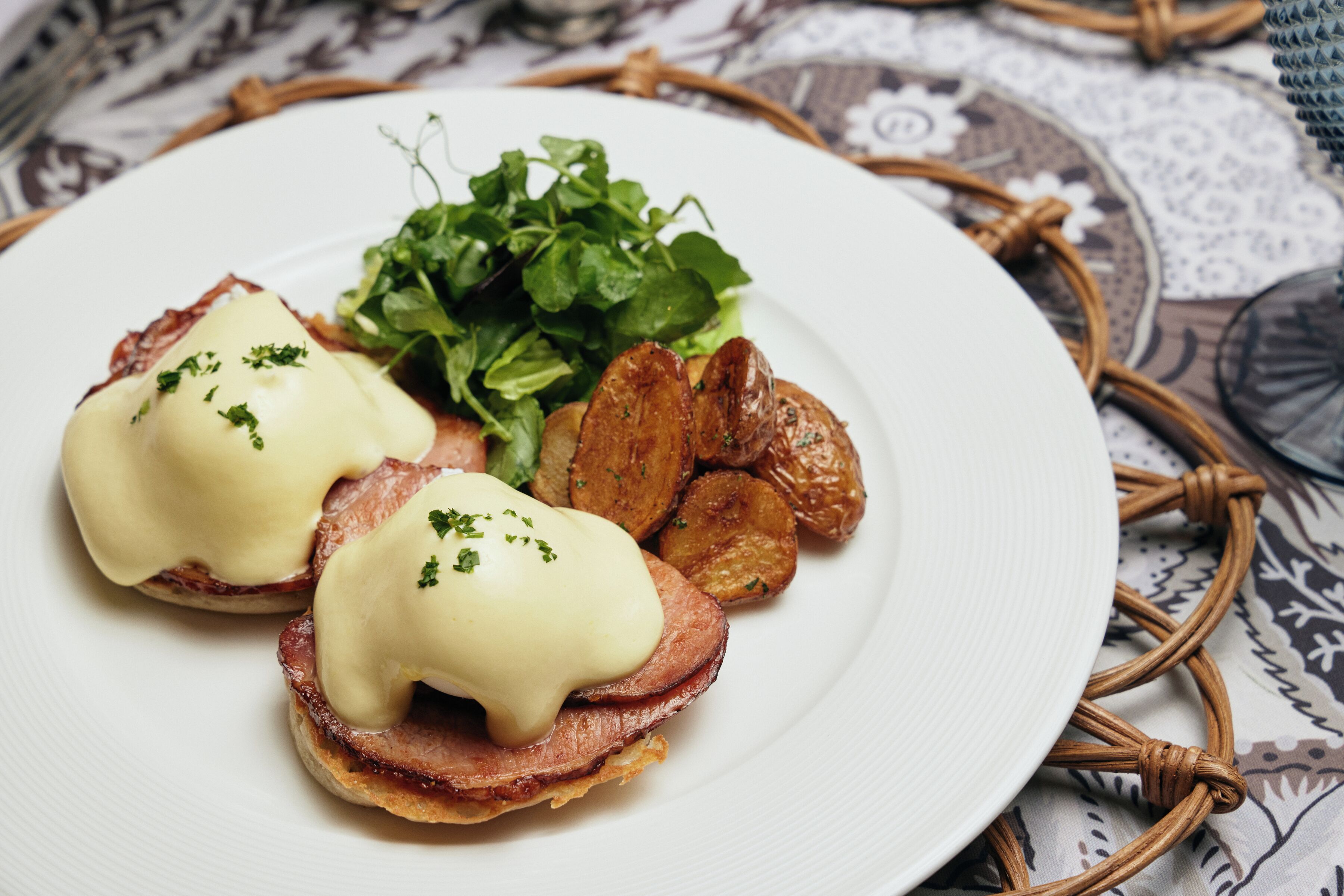 Um prato com ovos Benedict, batatas assadas e uma salada.