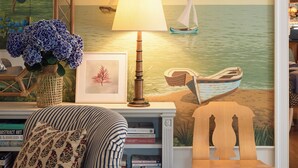 Une pièce comprenant une bibliothèque, un fauteuil, une lampe et une fresque murale représentant une scène de plage.