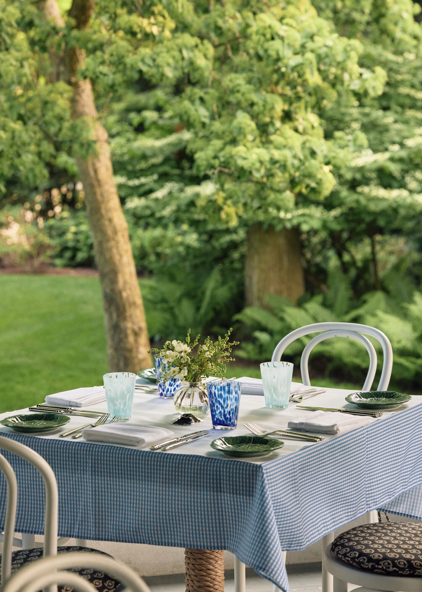 A table set outdoors with a checkered tablecloth, glassware, and cutlery.