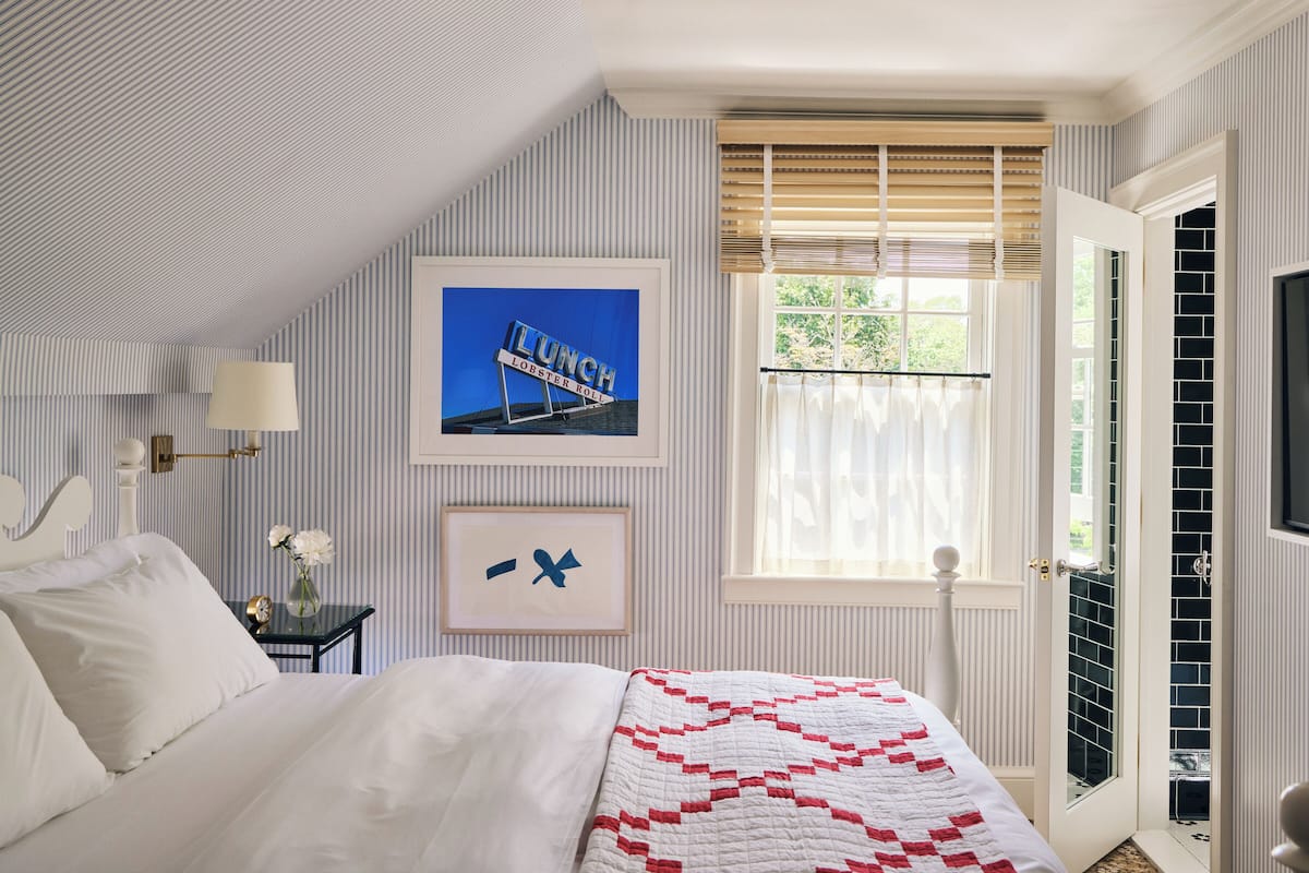 A bedroom with a bed, a nightstand, a lamp, a framed picture, and a window with blinds.