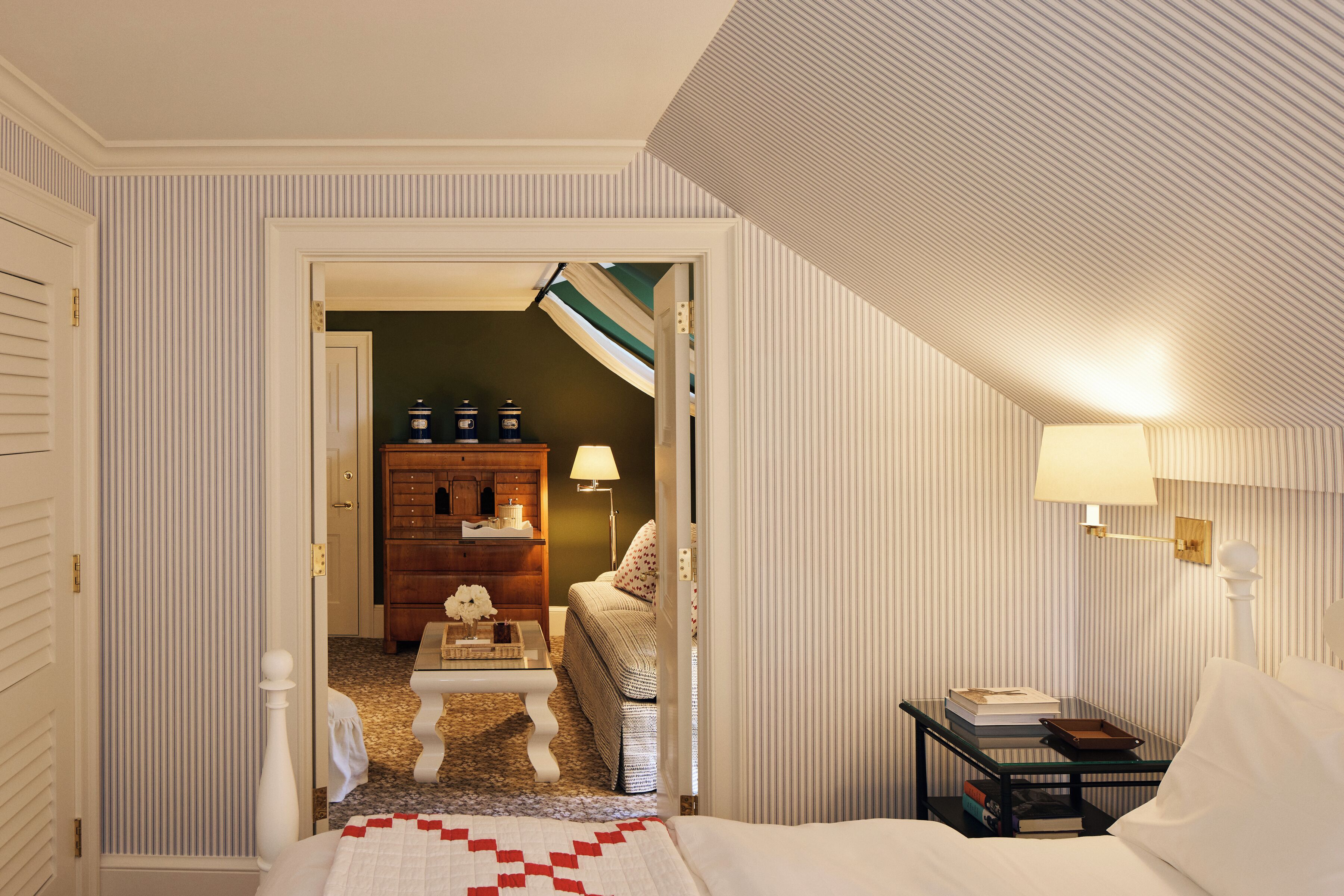 Une chambre d’hôtel comprenant un lit, une table de chevet avec une lampe, une commode et une petite table avec une lampe.