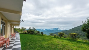 A hotel with a checkered outdoor seating area, a view of mountains, and a green lawn. - The Ayali Fernhill Resort, Chail (Kandaghat)