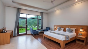 A hotel room with a large bed, a desk, and a chair. There is a window with a view of greenery outside. - The Ayali Fernhill Resort, Chail (Kandaghat)