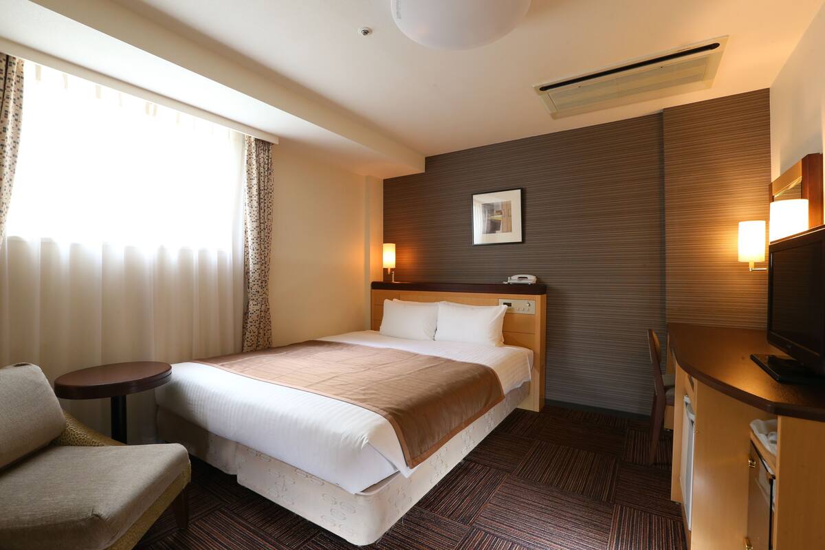 A hotel room with a large bed, a desk, a chair, a television, and a picture on the wall.