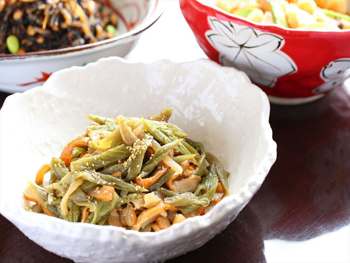 A bowl of seasoned vegetables, possibly a Korean dish, with a decorative red bowl in the background.