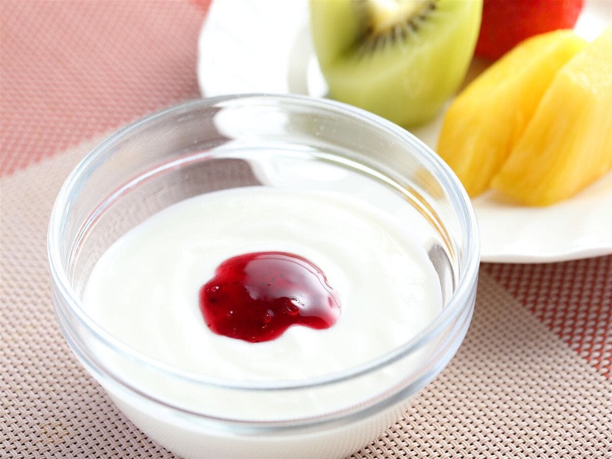 A clear glass bowl with a white substance and a red topping, placed on a woven mat.