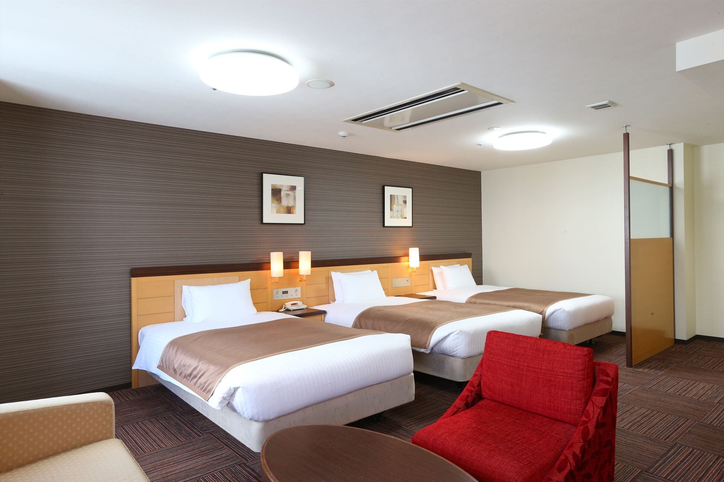 A hotel room with two beds, a red chair, and a wooden headboard.